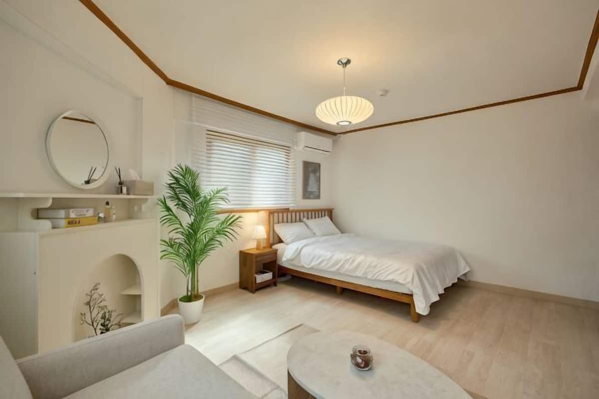 Une chambre à coucher avec un lit, une table de chevet, une lampe, une plante en pot et une petite table sur laquelle se trouve une tasse.