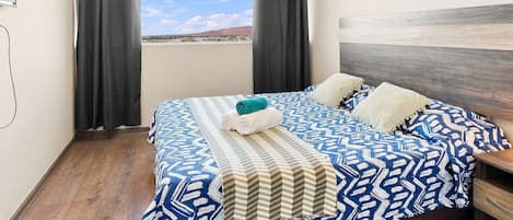 A hotel room with a bed, curtains, and a view of a landscape.