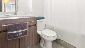 A bathroom with a white toilet, a wooden vanity with a towel, and a mirror above the sink. - Oceana Suites Concepto One (Calama)