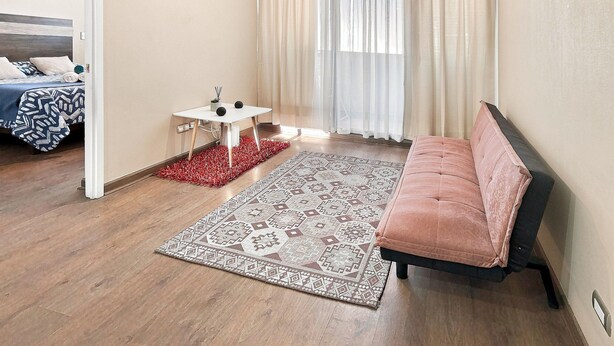 A room with a bed, a small table, a sofa, and a patterned rug. - Oceana Suites Concepto One (Calama)