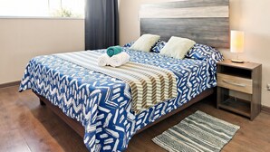 A hotel room with a bed, a nightstand, a lamp, and a patterned rug. - Oceana Suites Concepto One (Calama)