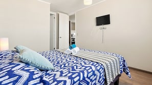 Une chambre à coucher avec un lit, un téléviseur fixé au mur et une porte donnant sur une autre pièce.