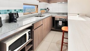 A modern kitchen with a built-in oven, microwave, and a window with a view. - Oceana Suites Concepto One (Calama)