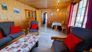 A cozy wooden interior with a sofa, armchairs, a dining table, and a quilt-covered coffee table.