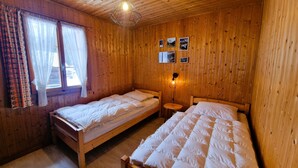 A wooden room with two beds, a window with curtains, and a wall-mounted lamp.