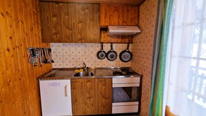 A compact kitchen with wooden cabinets, a white refrigerator, a stove, and three hanging frying pans.