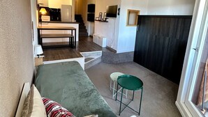 Ein kompakter Wohnbereich mit einer Couch, einem kleinen Esstisch, einer Küchenzeile und einer Treppe zu einer erhöhten Ebene.
