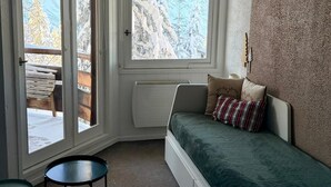 Ein Eckschlafzimmer mit Bett, einem kleinen Tisch und einem Fenster mit Blick auf schneebedeckte Bäume.