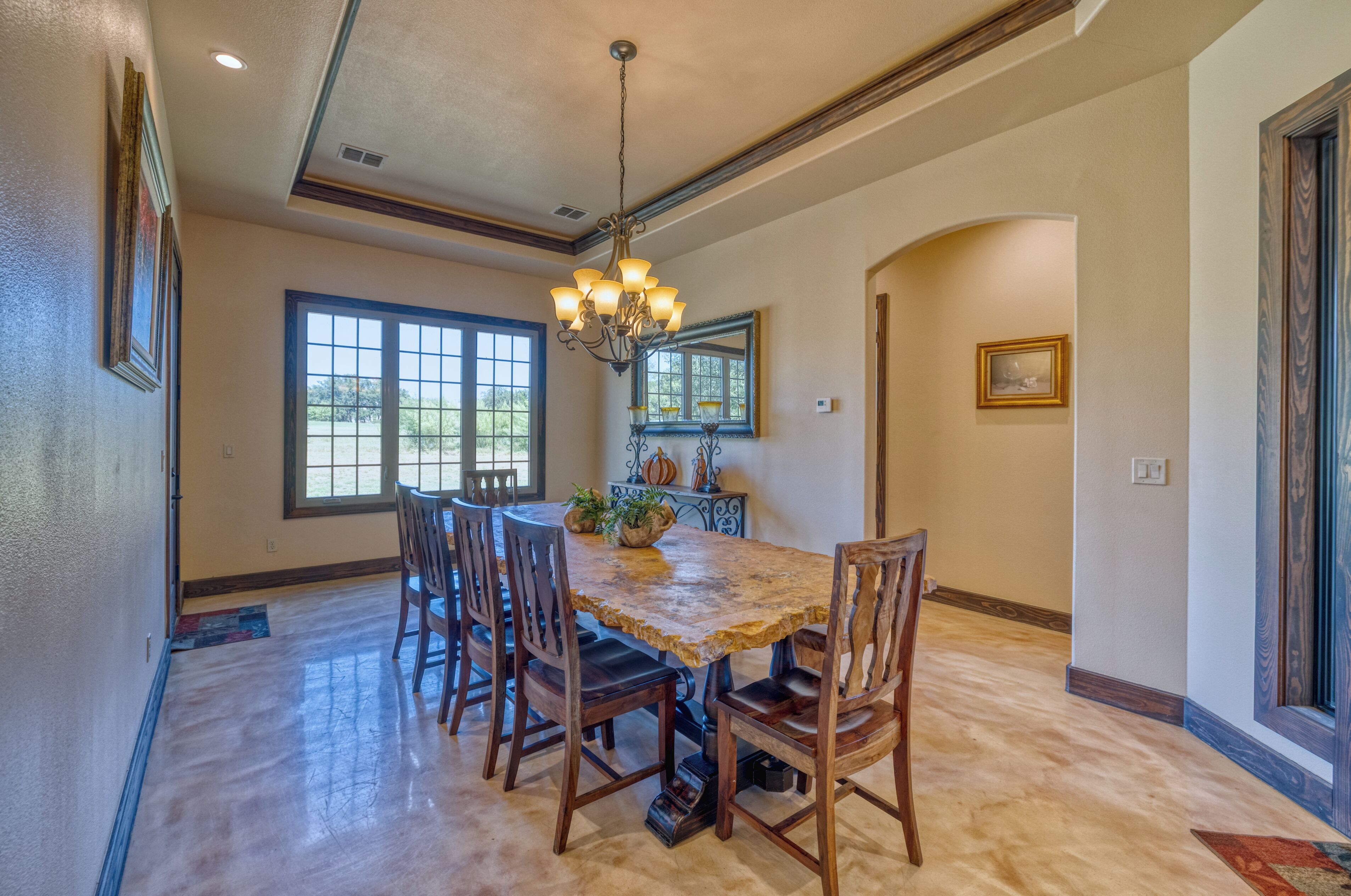A dining area with a wooden table and chairs, a chandelier, and a large window.