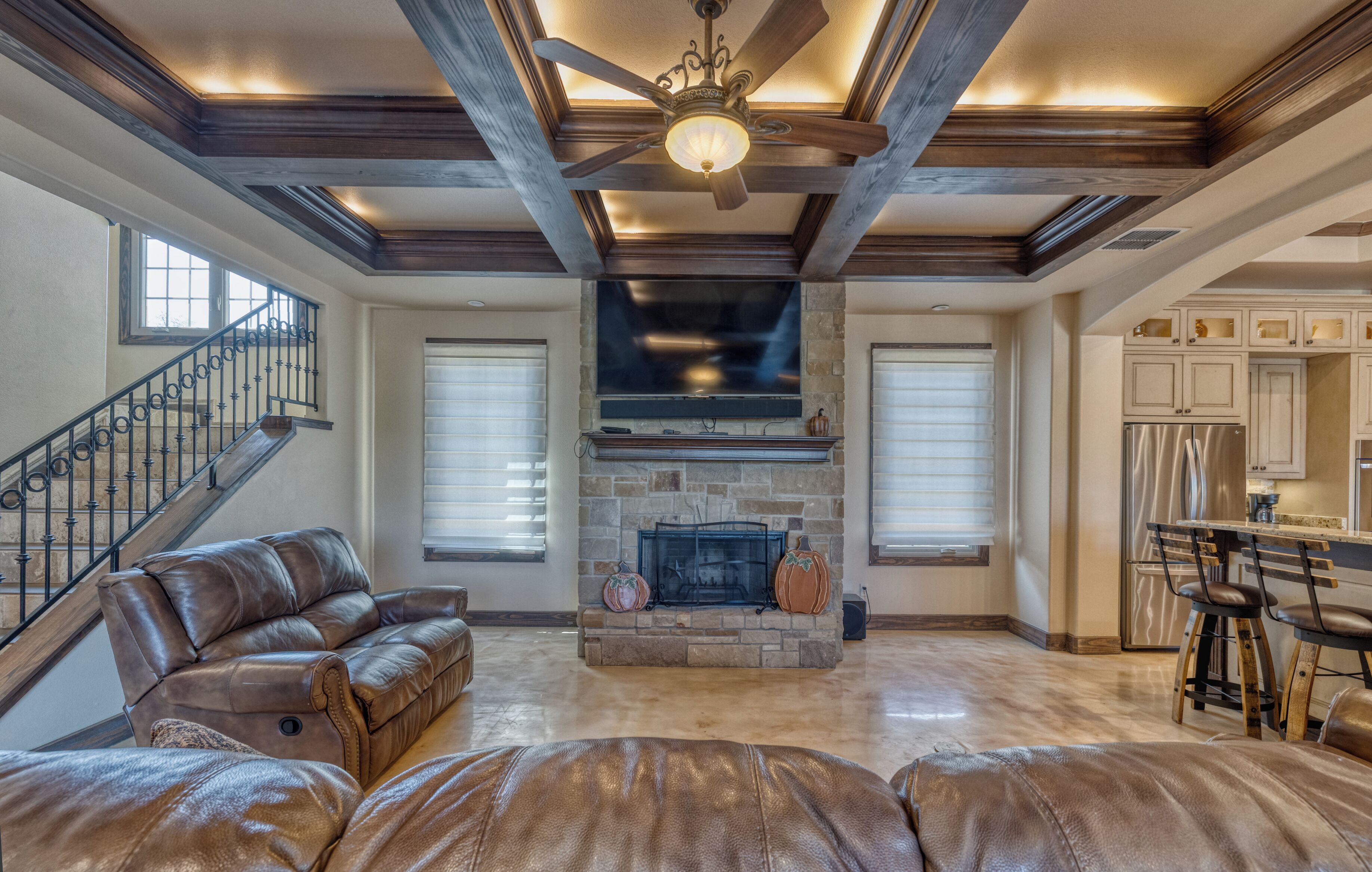 A spacious living room with a stone fireplace, leather sofas, and a wooden ceiling with exposed beams.