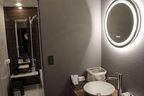 A bathroom with a round mirror, a sink, a shower, and a toilet.