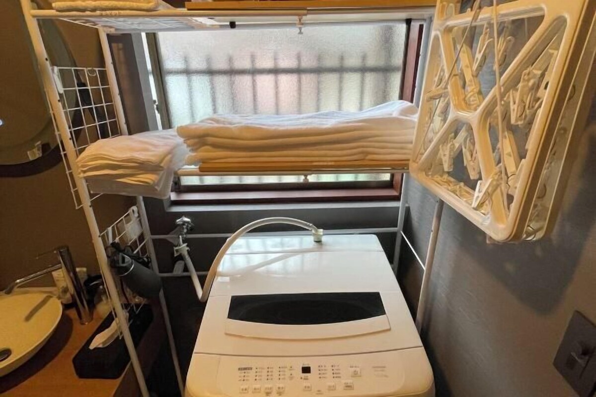 Ein kleines Hotelzimmer mit Bett, Waschmaschine und einem Fenster mit Jalousien.
