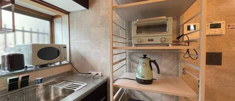 A compact kitchenette with a microwave, toaster, kettle, and a small refrigerator.