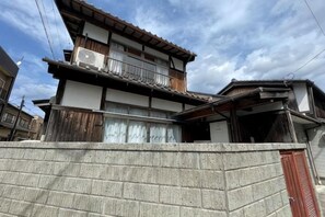 A traditional Japanese house with a wooden balcony, a concrete wall in the foreground, and a clear sky. - KYOTO TANGO MIYAZU inn (Miyazu)