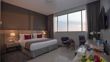 A hotel room with a large bed, bedside tables, a desk with a chair, a TV, and a view of the city.