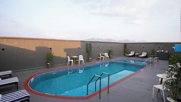 Un espace piscine aménagé sur le toit, avec des chaises longues, une piscine et une vue sur les montagnes.