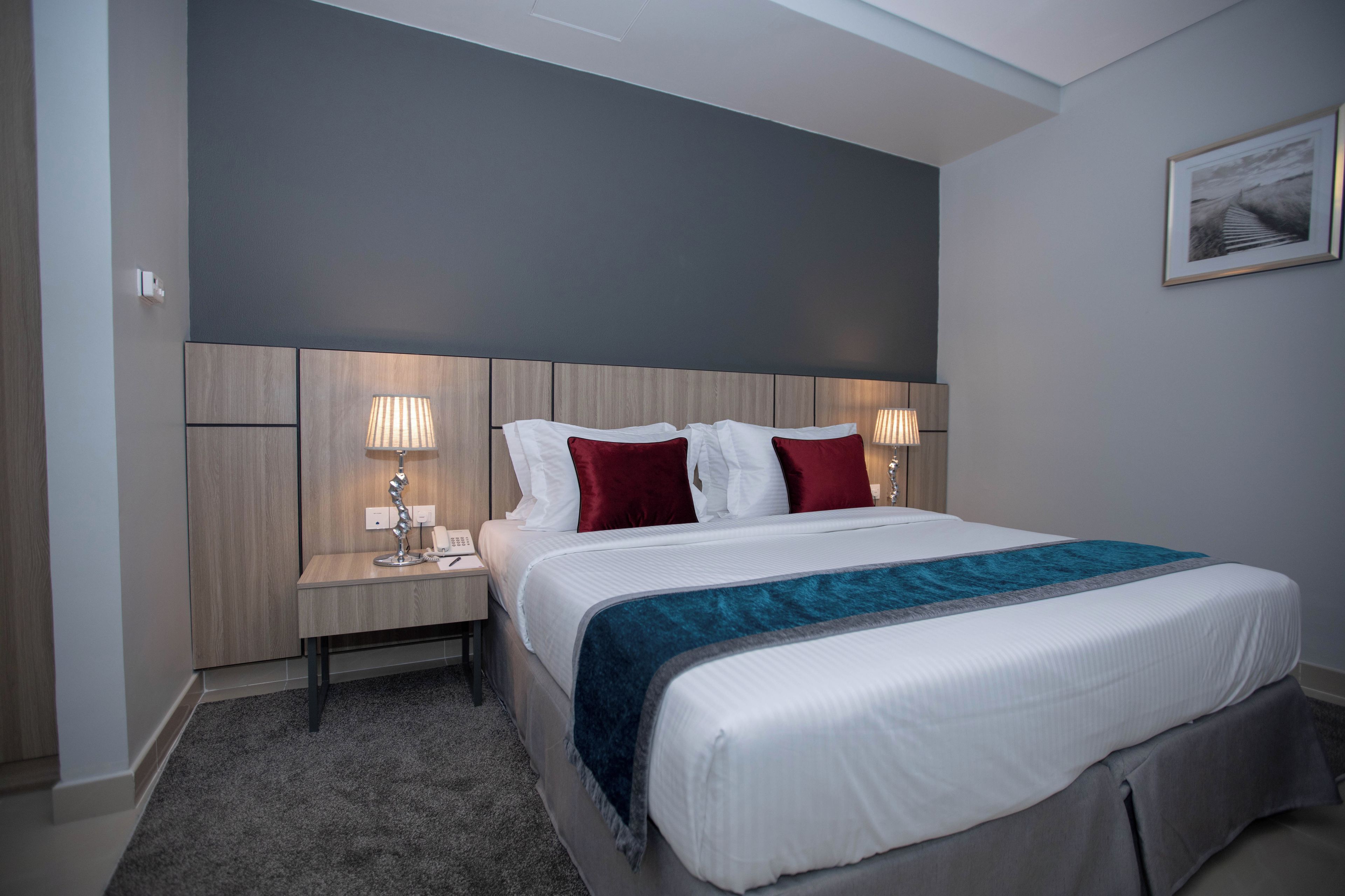 A hotel room with a large bed, two bedside tables with lamps, a headboard, and a framed picture on the wall.