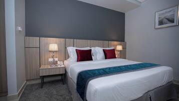 A hotel room with a large bed, two bedside tables with lamps, a headboard, and a framed picture on the wall.