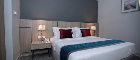 A hotel room with a large bed, two bedside tables with lamps, a headboard, and a framed picture on the wall.