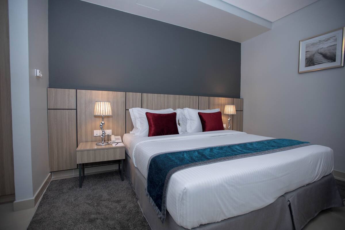 A hotel room with a large bed, two bedside tables with lamps, a headboard, and a framed picture on the wall.