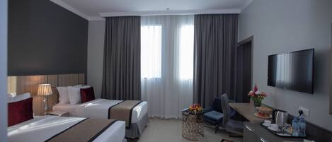 A hotel room with two beds, a desk, a TV, and a dining area.