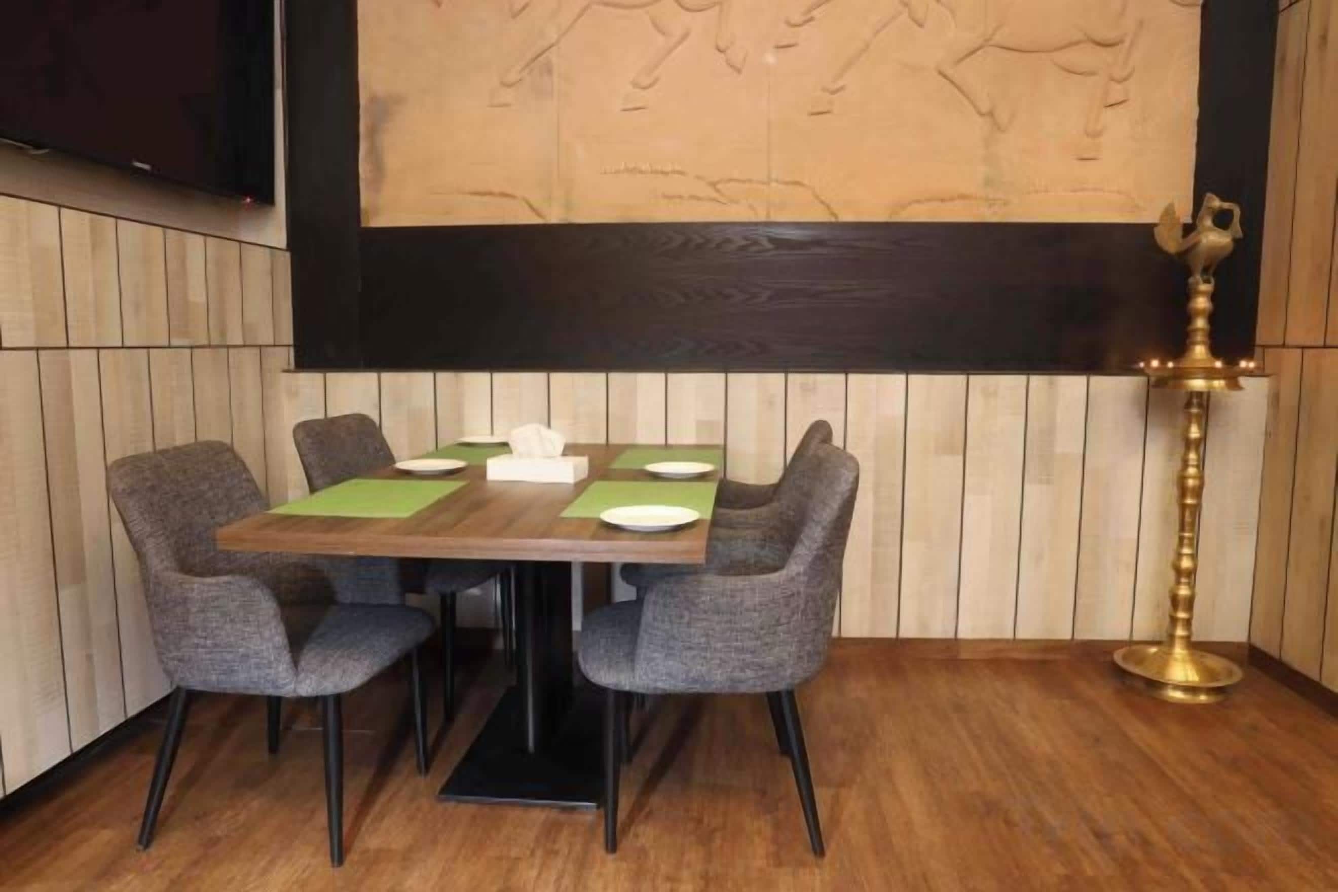 A dining area with a wooden table, four grey chairs, and a brass lamp.