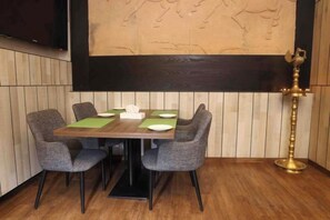 A dining area with a wooden table, four grey chairs, and a brass lamp. - Fortis Hotel Fujairah (Al-Fujairah)