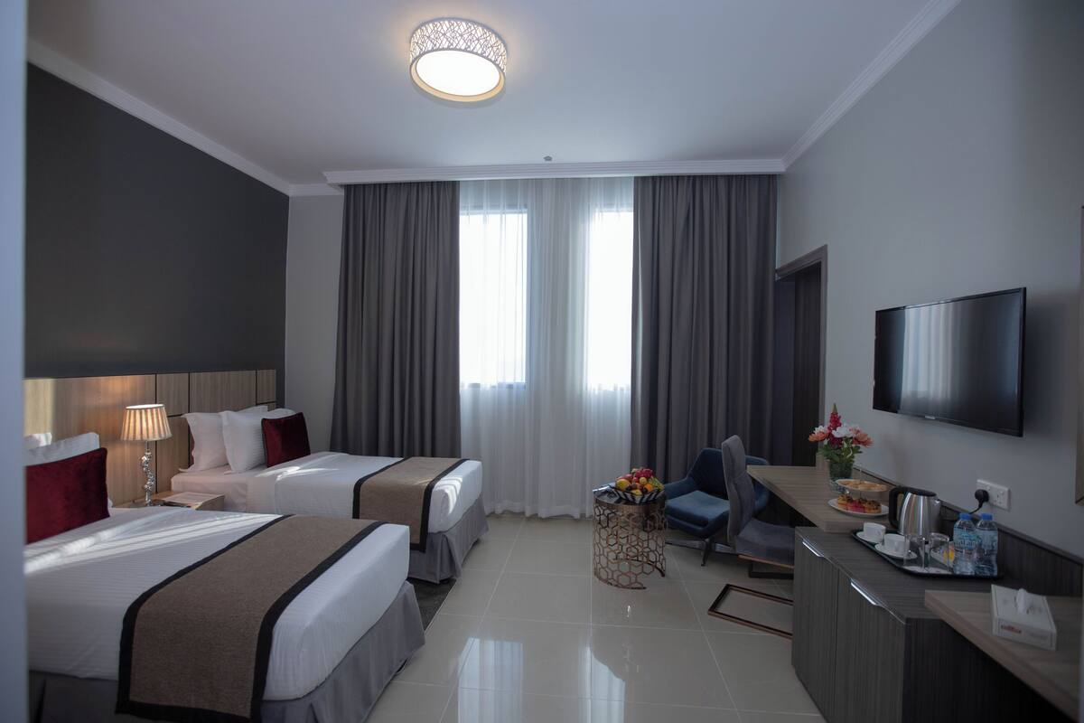 A hotel room with two beds, a desk, a TV, and a dining area.