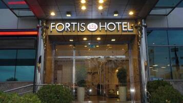 The exterior of Fortis Hotel with a glass entrance and a sign above.