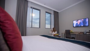A hotel room with a bed, a desk, a television, and a window with curtains. - Fortis Hotel Fujairah (Al-Fujairah)