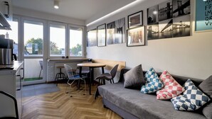 A modern living room with a sofa, chairs, a dining table, and a kitchen area. - RentPlanet - Apartament plac Nowy Targ (Wrocław)