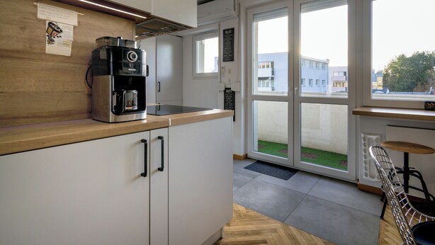 A modern kitchen with a coffee maker, cabinets, and a view of the outside through large windows. - RentPlanet - Apartament plac Nowy Targ (Wrocław)