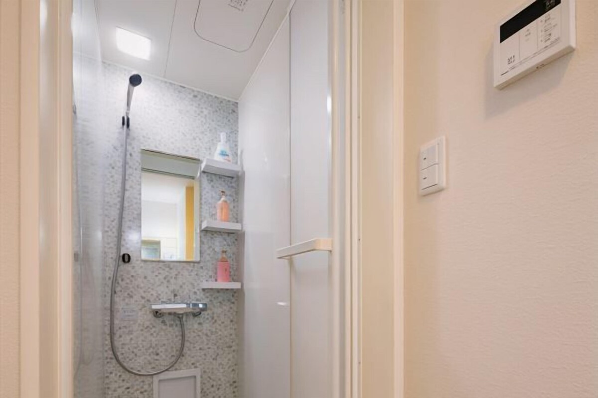 A bathroom with a shower, a mirror, and a wall-mounted shelf with toiletries.