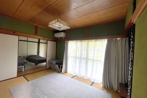 Een traditionele Japanse kamer met tatami vloeren, een futonbed, schuifdeuren en een groot raam met gordijnen.