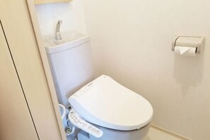 Un water bianco con un pannello di controllo, un lavandino e un portasciugamani di carta a parete.