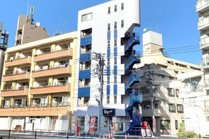 A multi-story building with balconies, a storefront, and a blue staircase. - SunStay Fudomae (Tokyo)