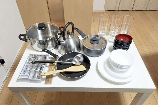 Uma mesa com utensílios de cozinha, incluindo panelas, frigideiras, colheres, pratos e copos.