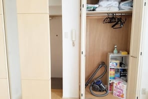 Habitación de hotel con armario, estante pequeño con artículos de aseo y aspiradora.