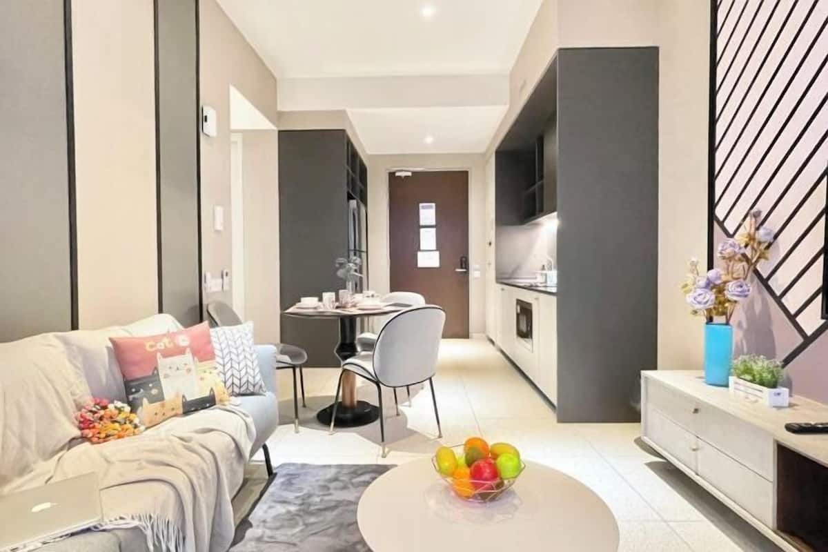 A modern living room with a sofa, a dining table, and a kitchen area in the background.