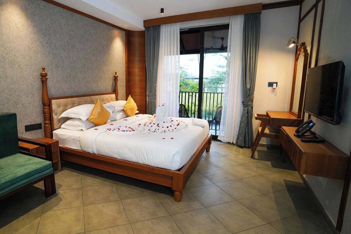 A hotel room with a four-poster bed, a green sofa, a desk with a phone, and a TV on the wall.