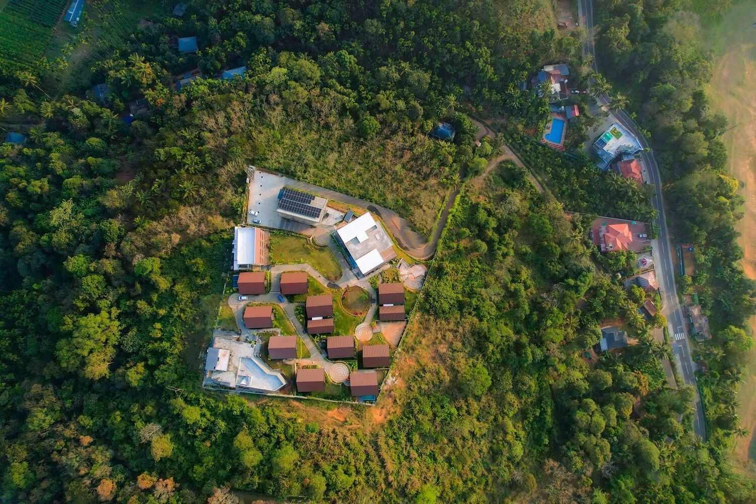 An aerial view of a residential area with multiple houses, a central building with solar panels, and a road.