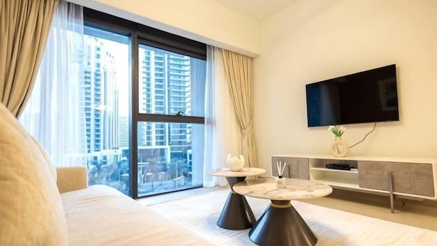 Quarto de hotel moderno com uma cama grande, uma mesa de jantar, televisão de tela plana e vista para edifícios altos.