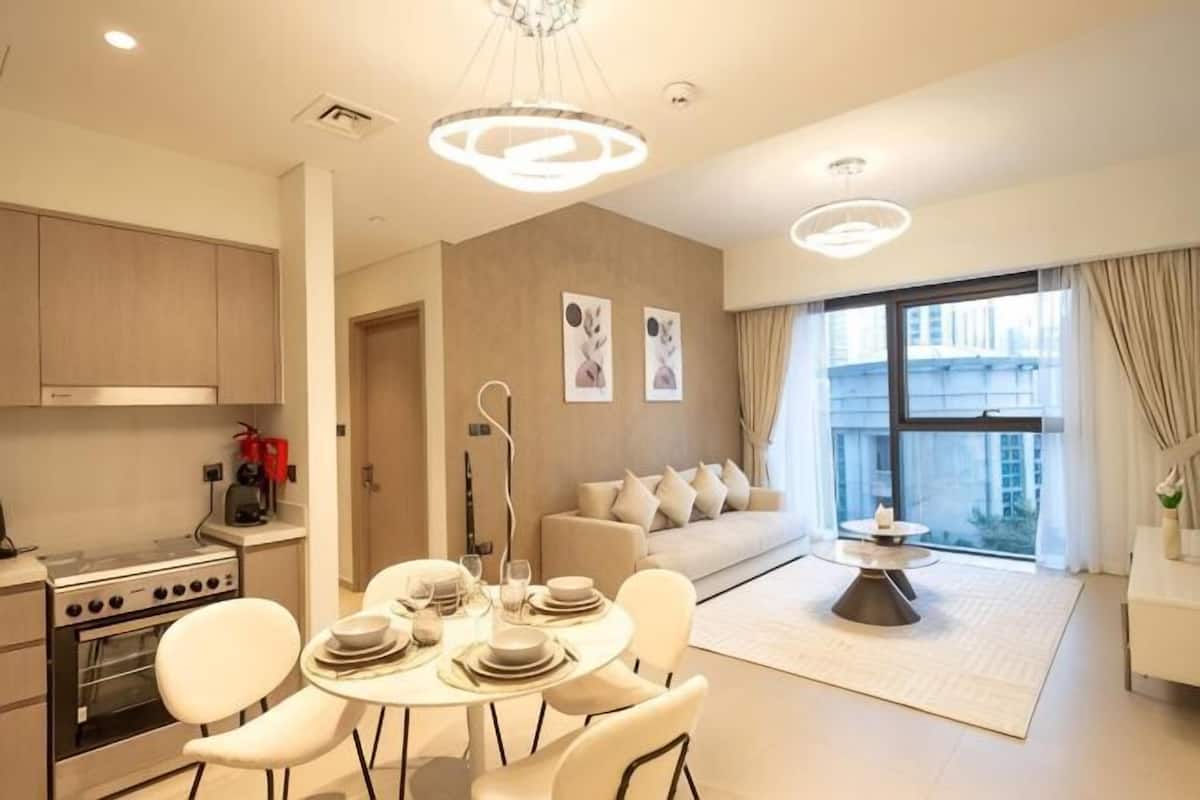 A modern kitchen with a dining area, a sofa, and a large window with curtains.