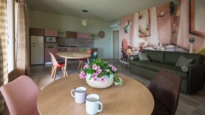 Uma sala de estar moderna com uma mesa redonda de madeira, duas canecas brancas, um sofá verde e um mural abstrato colorido na parede.