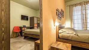 Quarto com cama de madeira, uma cadeira vermelha, cômoda e televisão na parede.
