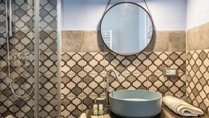 A bathroom with a glass shower enclosure, a round sink with a blue basin, and a mirror on the wall. - Apartment No. 4 ( CIN: IT008031B48RJTC5CL Citra 008031-LT-1323 ) (Imperia)
