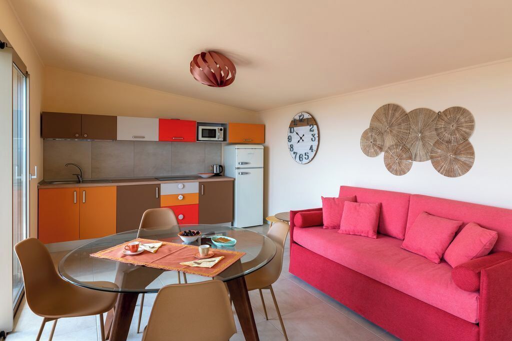 Un espace de vie compact comprenant un coin cuisine, un coin repas et un canapé rouge.
