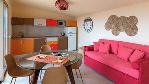 Un espacio habitable compacto con kitchenette, zona de comedor y sofá rojo.