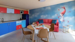 Una cocina moderna con armarios rojos y azules, una zona de comedor con un sofá rojo y un mural de una niña y pájaros.