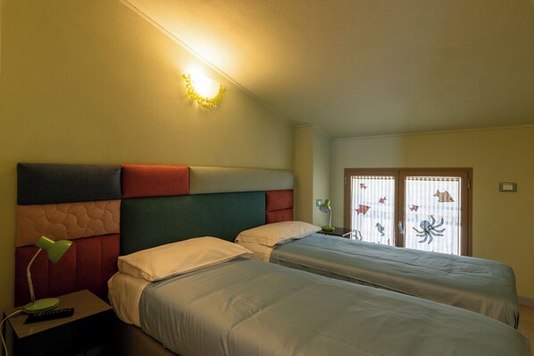 A hotel room with two beds, a nightstand with a lamp, and a window with curtains.